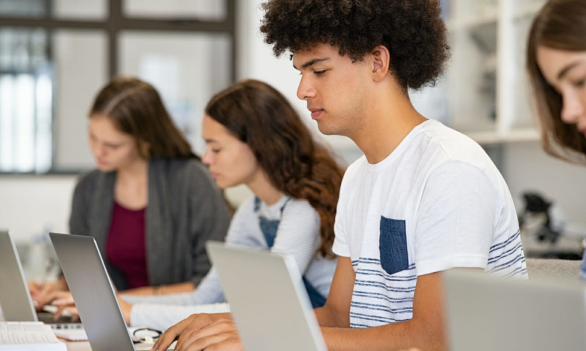 College student using laptop in class during computer lesson. Side view of guy sitting in a row studying in classroom on pc. Black high school student studying on laptop in university library.