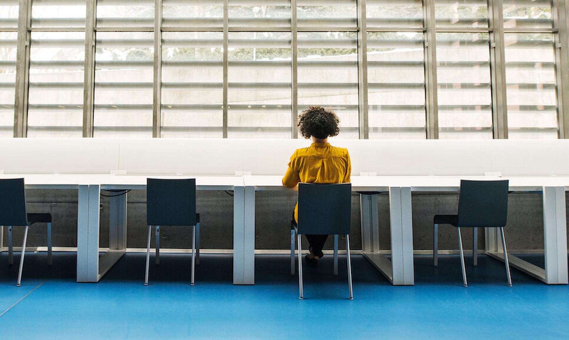 Rear view of young student or businesswoman sitting on desk in room in a library or office.