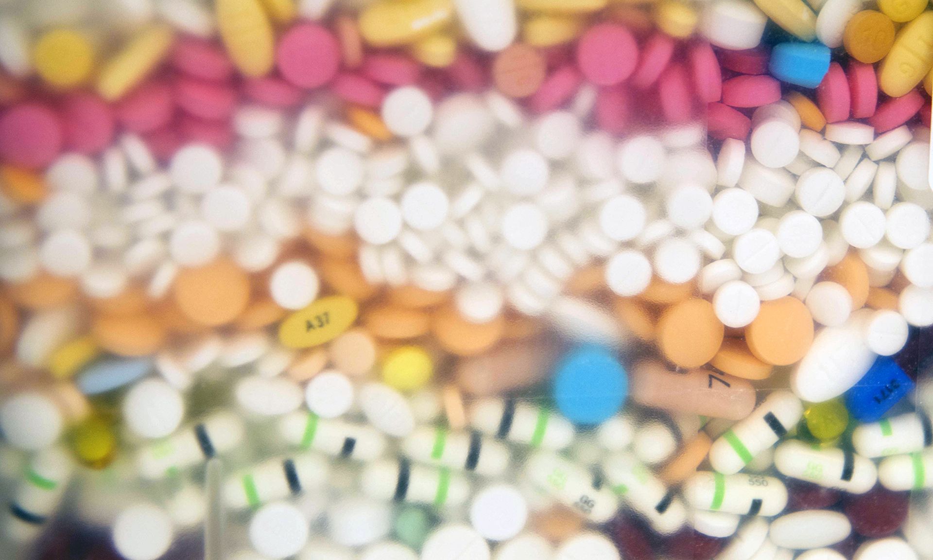 Multiple layers of pills of different colors sit in a pharmacy's pill disposal container.