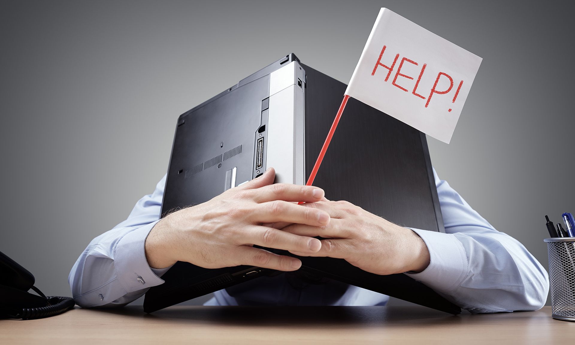 Frustrated and overworked businessman burying his head uner a laptop computer asking for help