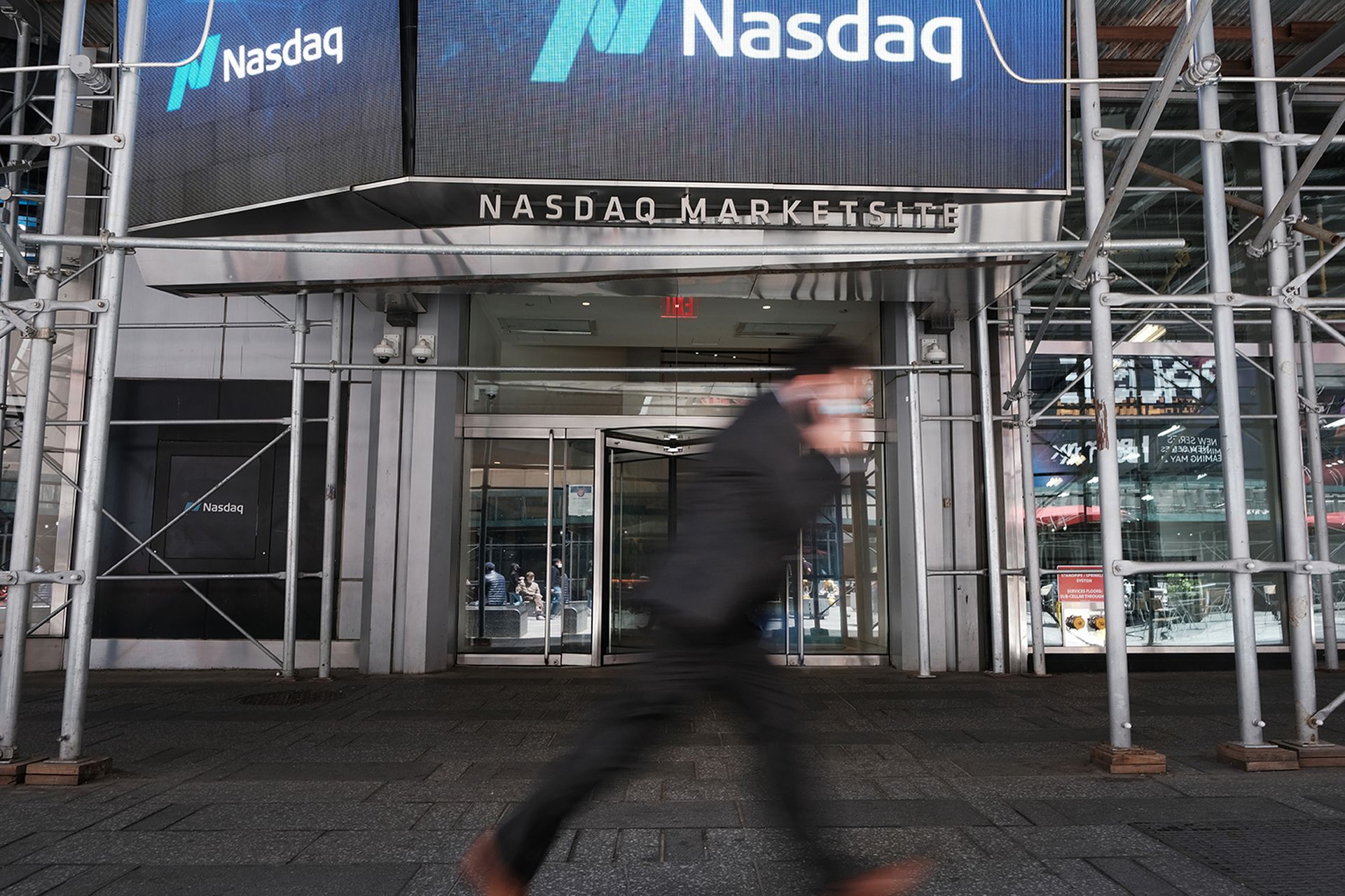People walk by the Nasdaq Composite site in Times Square on May 11, 2021, in New York City. In spite of current market trends, security company ZeroFox began trading on the Nasdaq on Aug. 4. (Photo by Spencer Platt/Getty Images)