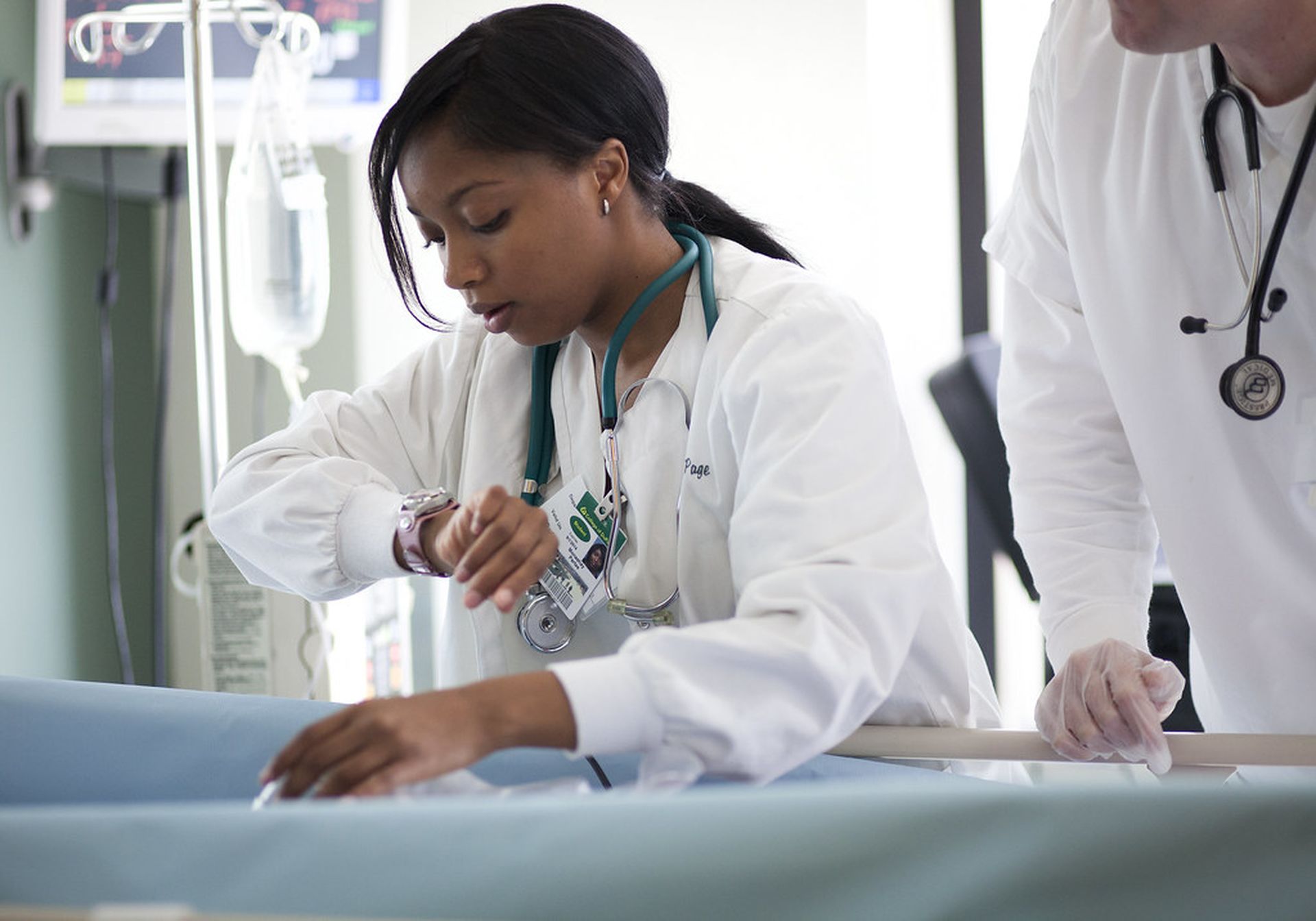 A nurse looks at her watch at the bedside of a patient
