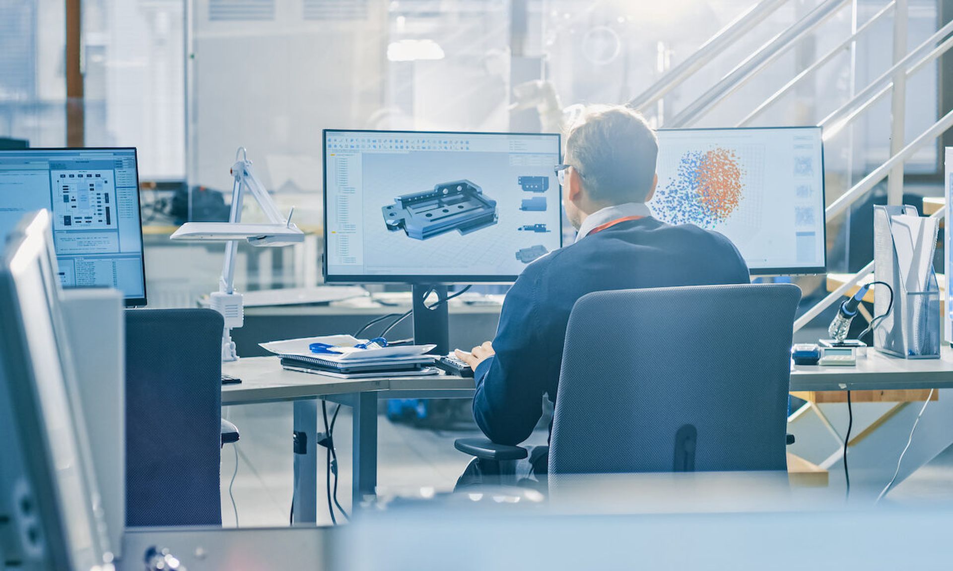 Back View of Industrial Engineer Working on Desktop Computer in Bright Office. Screens Show IDE / CAD Software, Implementation of Machine Learning, Neural Networking and Cloud Computing