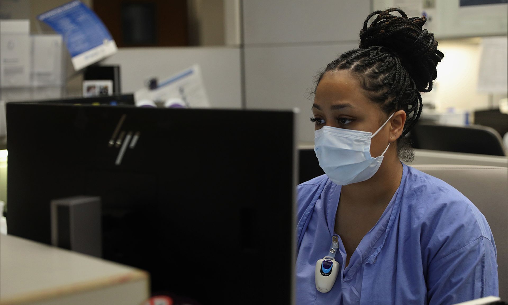 A nurse sits at a computer to review patient vital signs.