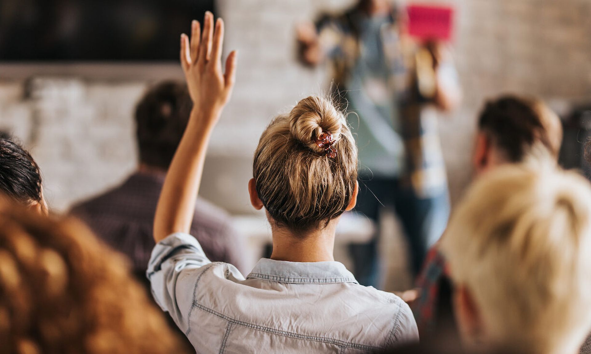 Rear view of casual businesswoman raising her hand to ask the question on education event in a board room.