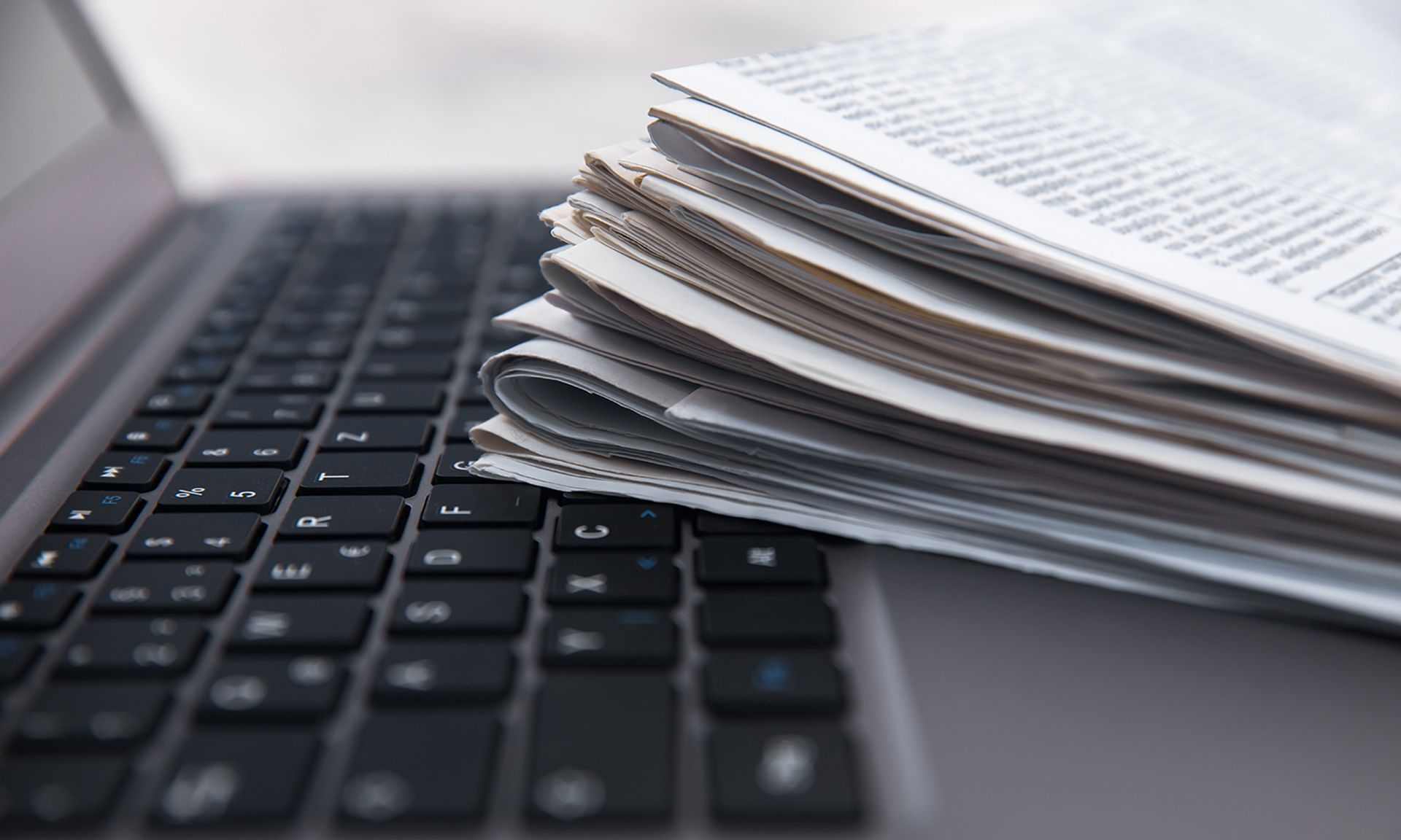 Pile of daily papers with news on the computer