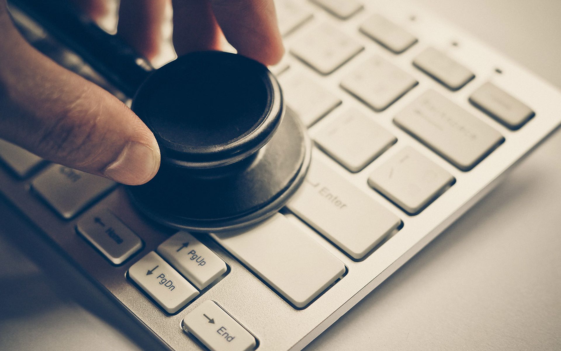 hand holding a stethoscope over computer keyboard