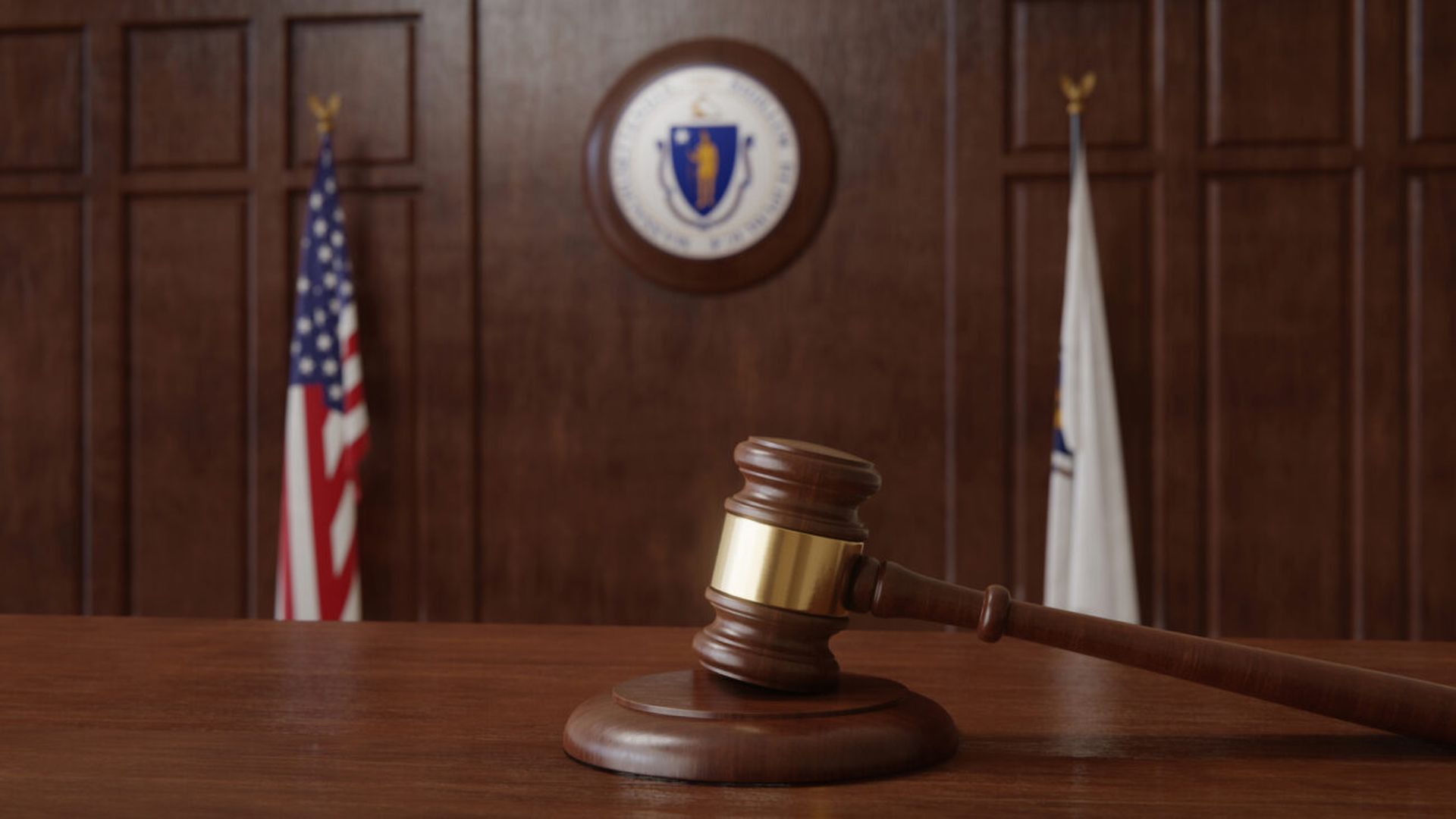 Courtroom scene with US flag and state seal and flag of the state of Massachusetts.