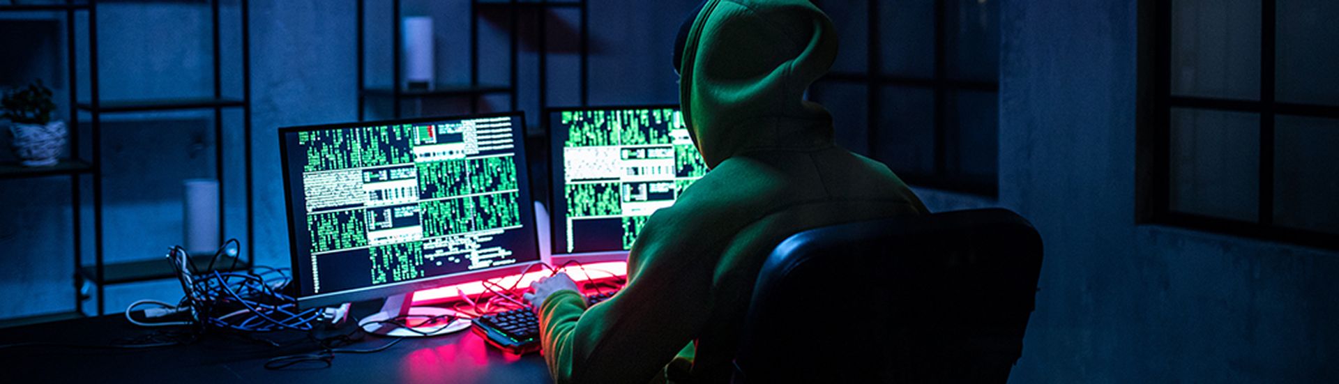 Hacker man working on computers alone in dark room, rear view.