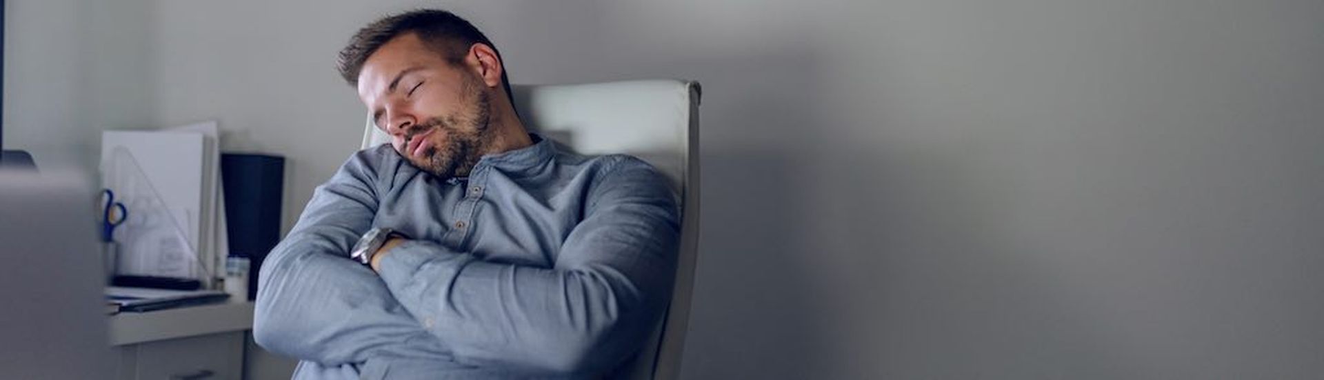 Tired handsome Caucasian bearded employee sleeping in the chair late at night in home office.