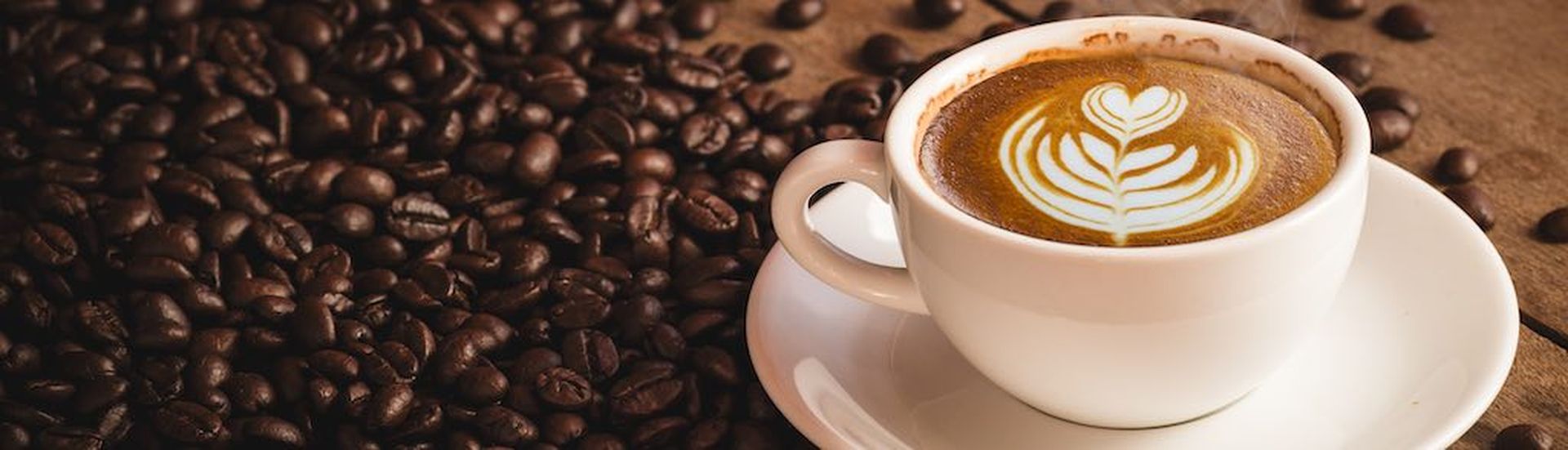 Coffee beans and Hot Cofee cup with latte art on wooden background. side view with copy space for your text