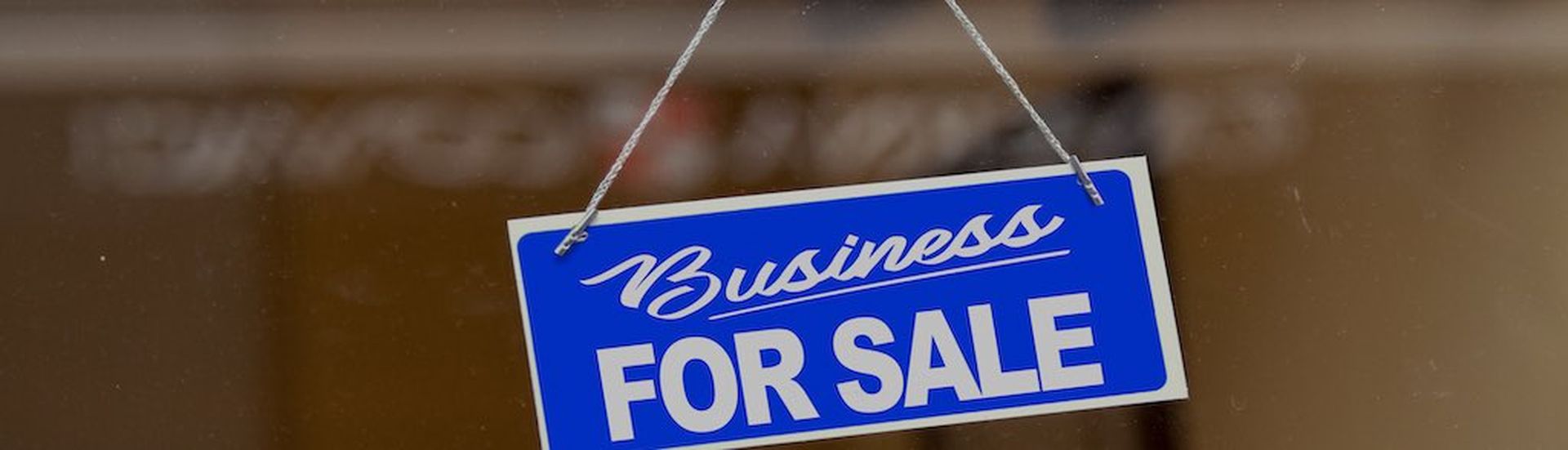 Orange sign hanging at the glass door of a shop saying: &#8220;Business for sale&#8221;.