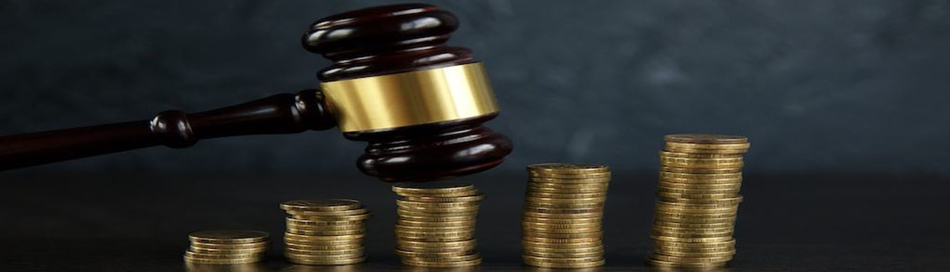 Close-up Of A Judge&#8217;s Hand Holding Gavel Over Stacked Golden Coins