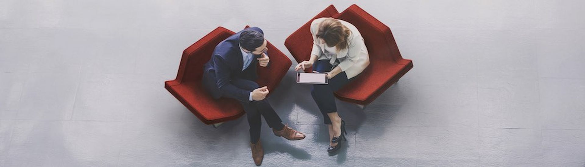 A high-angle view of a businessman and a businesswoman sitting in the office building lobby and using a tablet computer