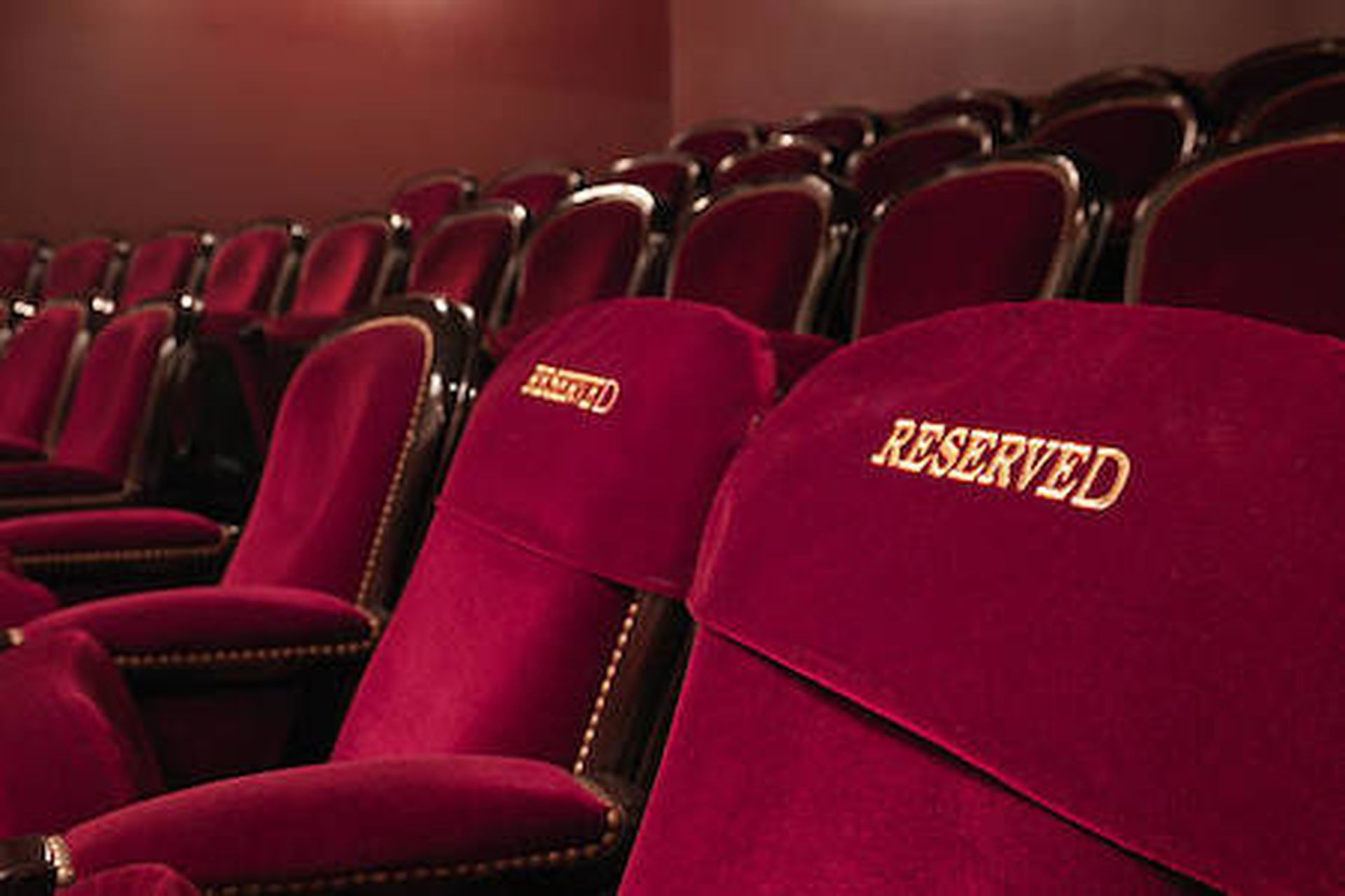 two red reserved theater seats side by side in the middle of others