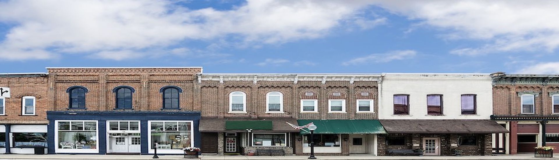 A photo of a typical small town main street in the United States of America. Features old brick buildings with specialty shops and restaurants. Decorated with spring flowers and American flags.