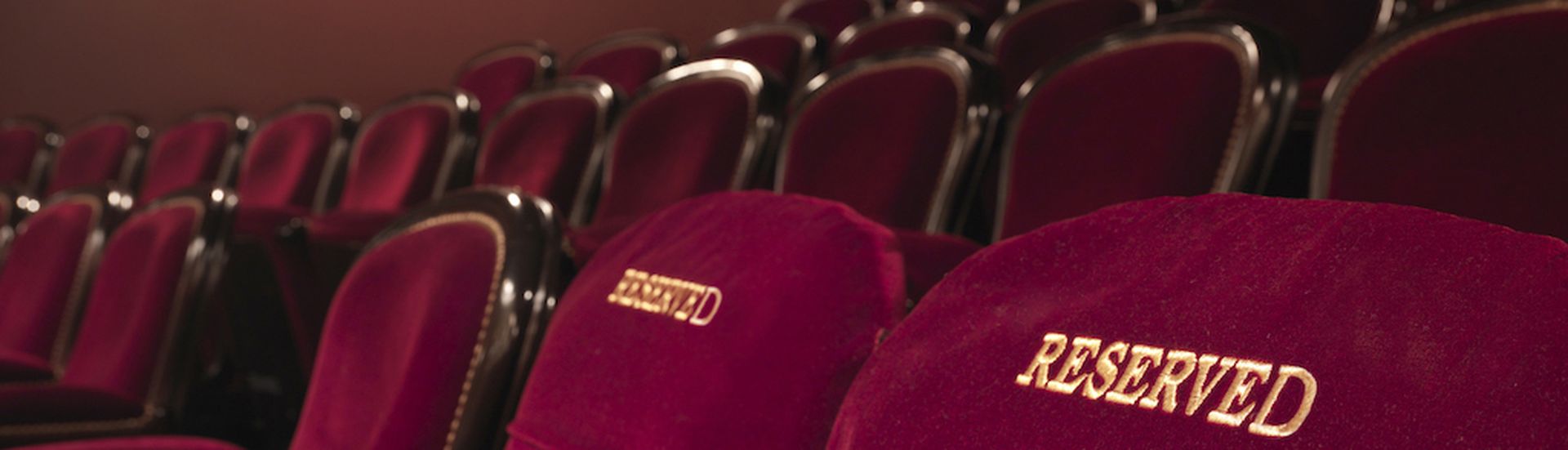 two red reserved theater seats side by side in the middle of others