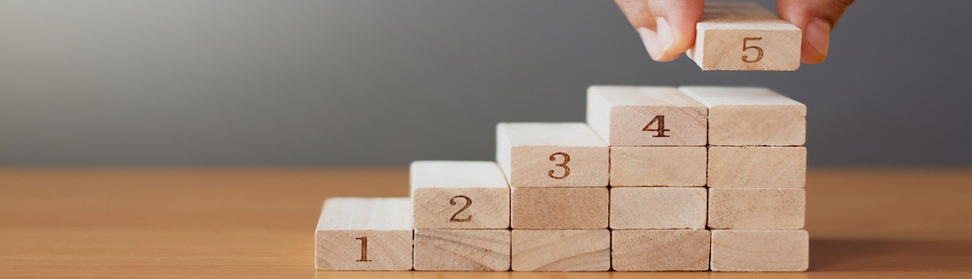 Women hand putting a wooden block on top and arranging wooden blocks stacking on wooden table  in the shape of a staircase, Business concept for growth success process.