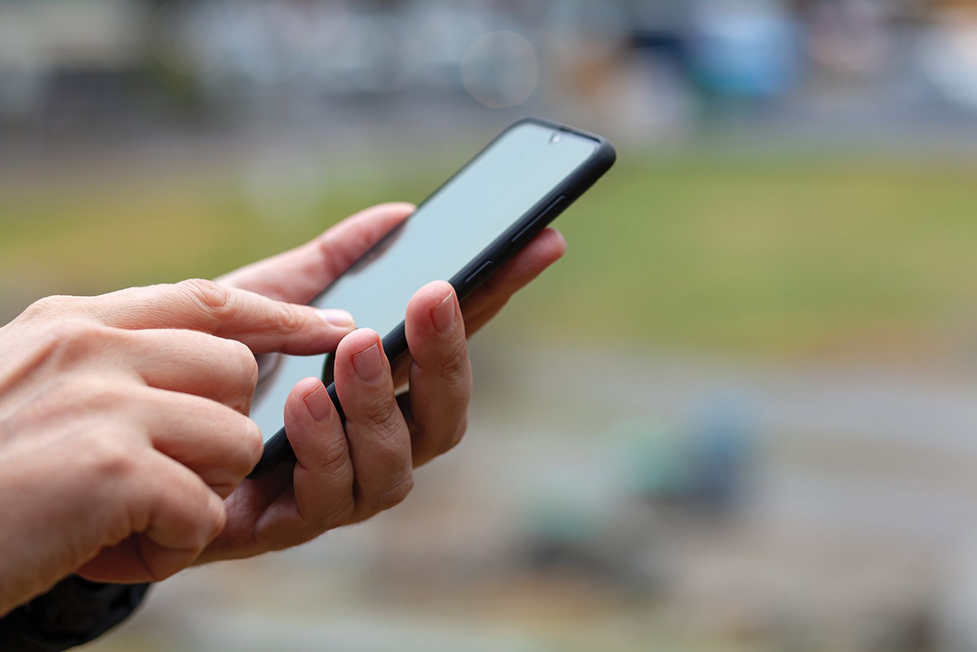 Male hand holding smart phone outside.