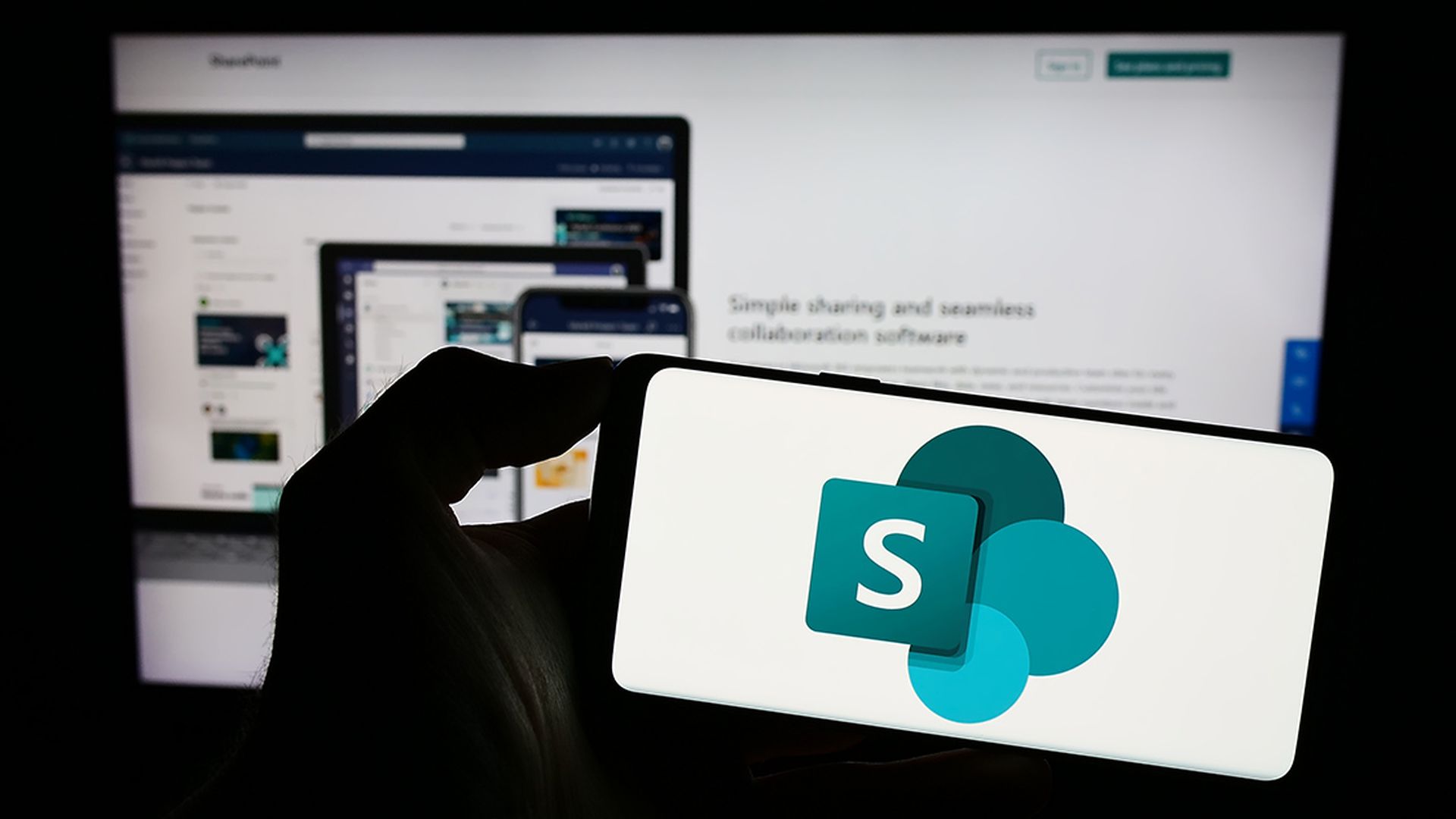 Person holding smartphone with logo of collaborative platform Microsoft SharePoint on screen in front of website. Focus on phone display.
