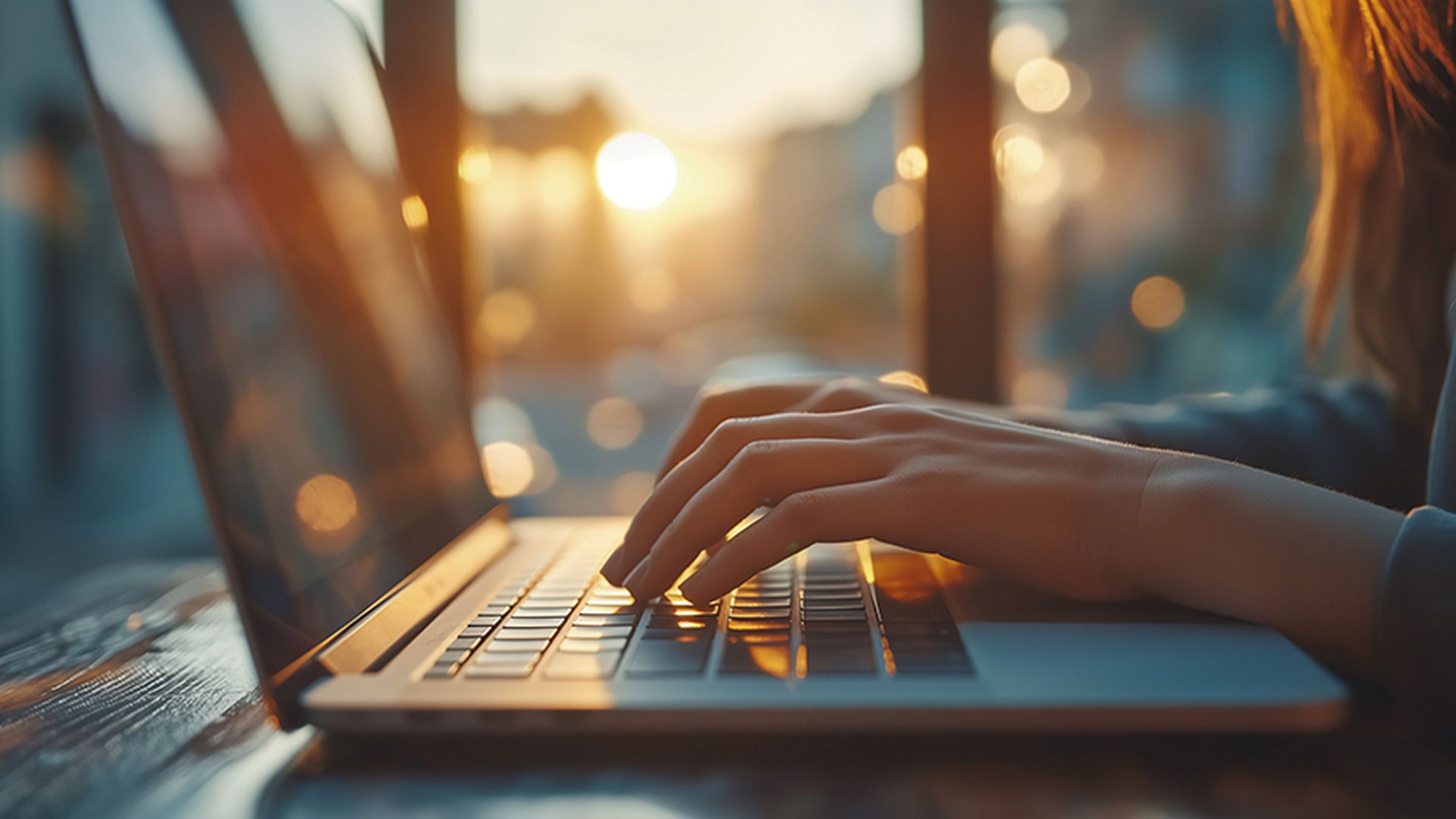 Close up of female hands typing on laptop keyboard, working at home, sunset in background