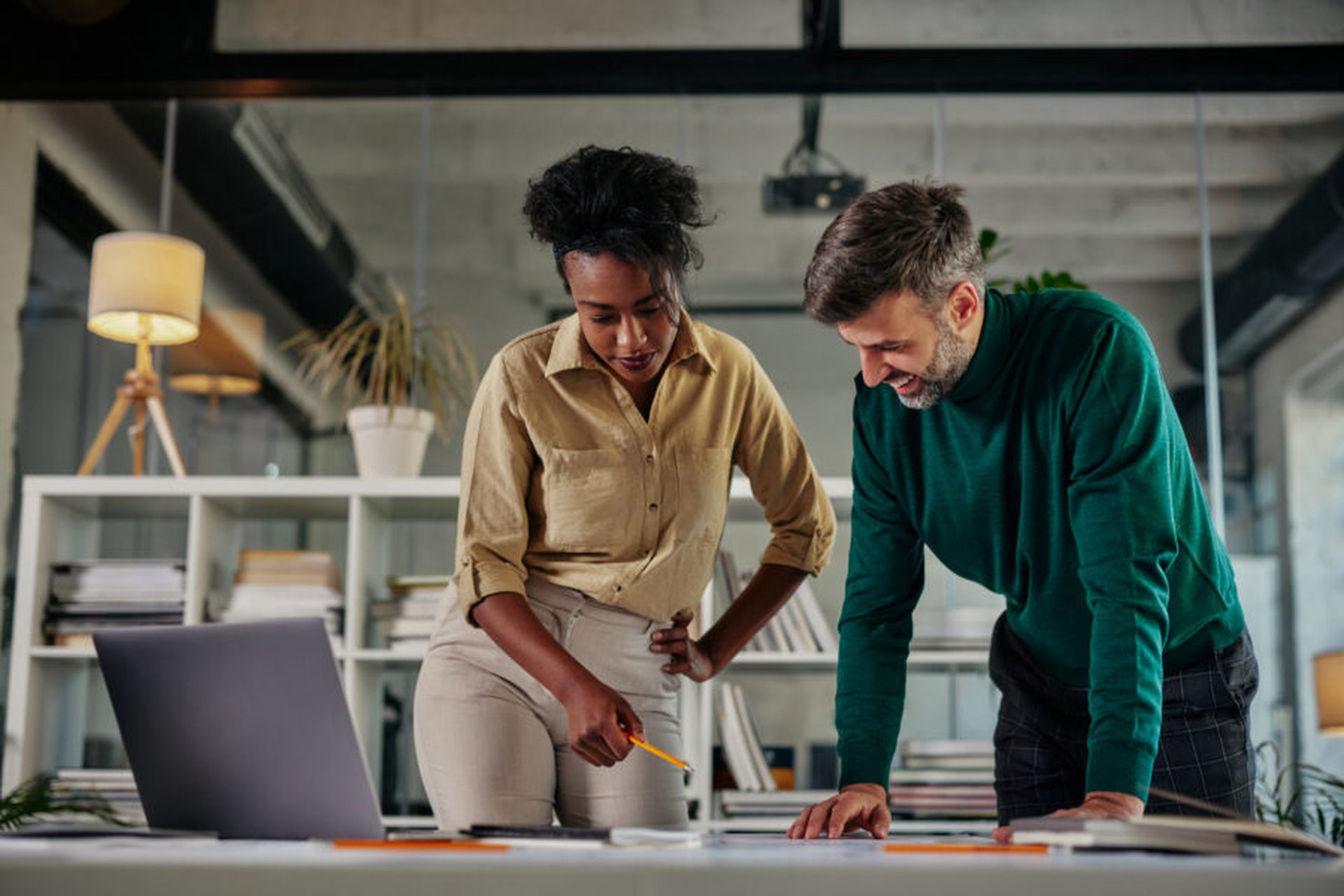 Two young multiracial business couple having a successful meeting in modern office. They are standing at the worktable and going through paperwork (Adobe Stock)