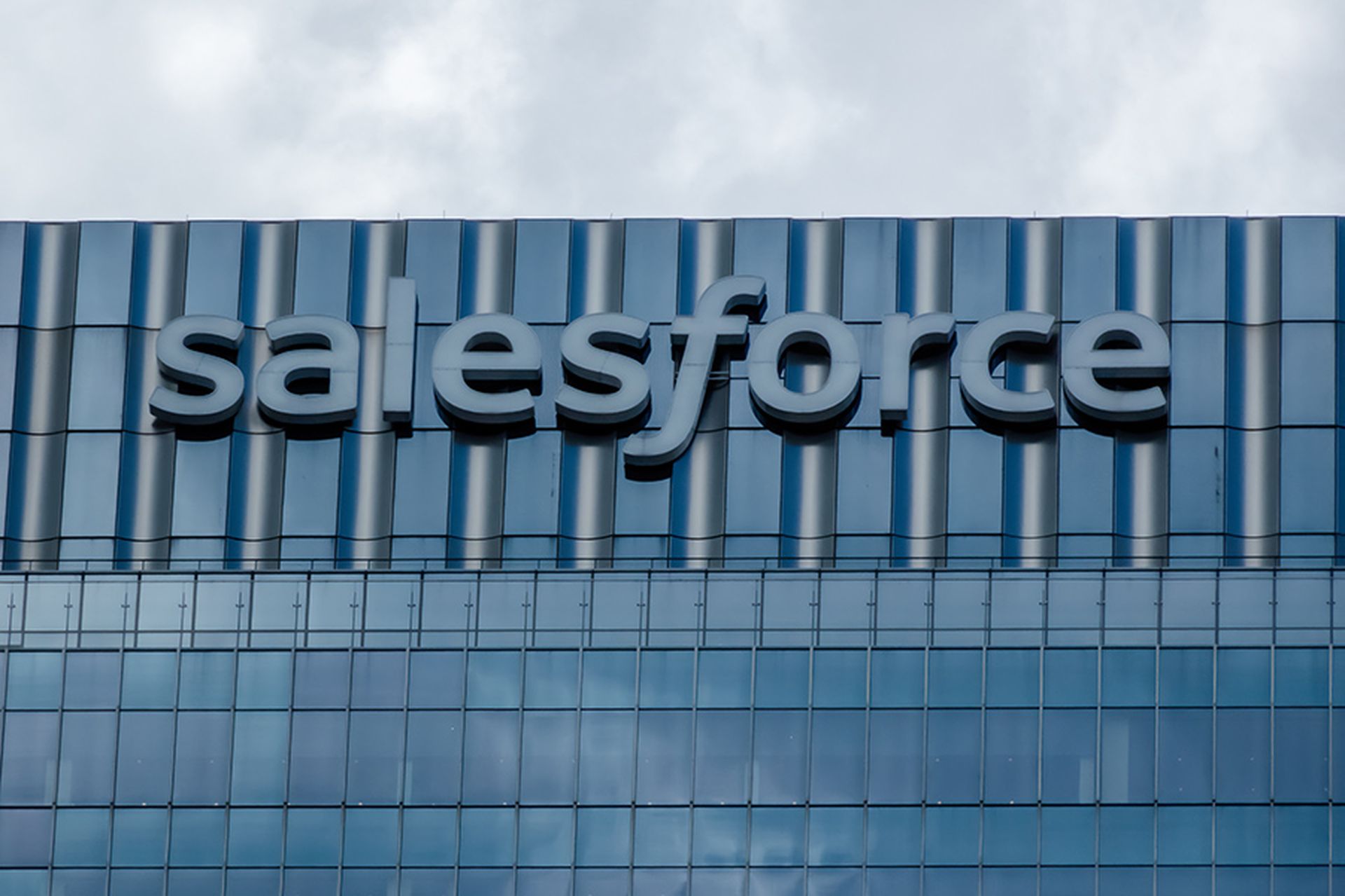 A close-up of the Salesforce sign on a modern glass and steel building, representing the technology industry, cloud computing, and corporate success.