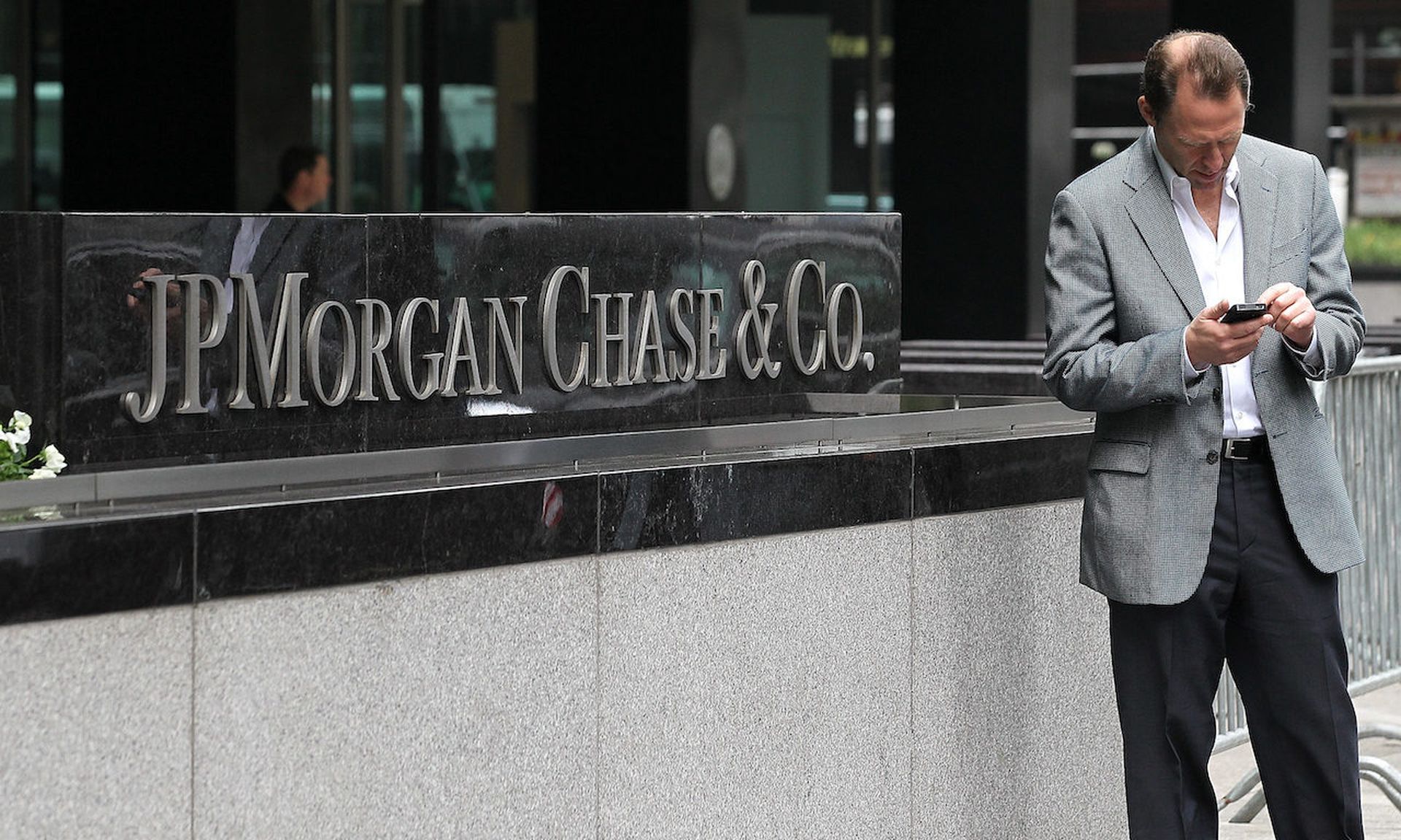 A pedestrian uses his cell phone by a sign outside of the JPMorgan Chase headquarters in New York City.  (Photo by Justin Sullivan/Getty Images)