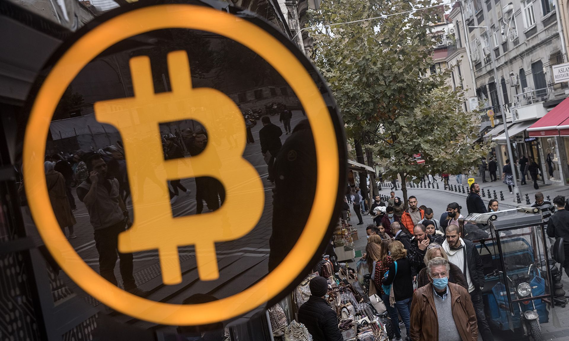 People walk past a Bitcoin symbol at the entrance of a cryptocurrency exchange office on Oct. 19, 2021, in Istanbul. (Photo by Chris McGrath/Getty Images)