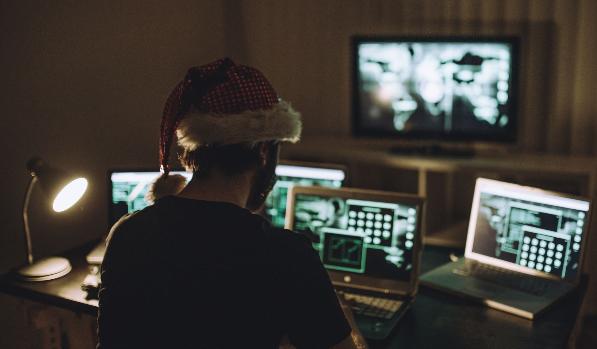 Computer hacker wearing santa hat while working on laptop late at night