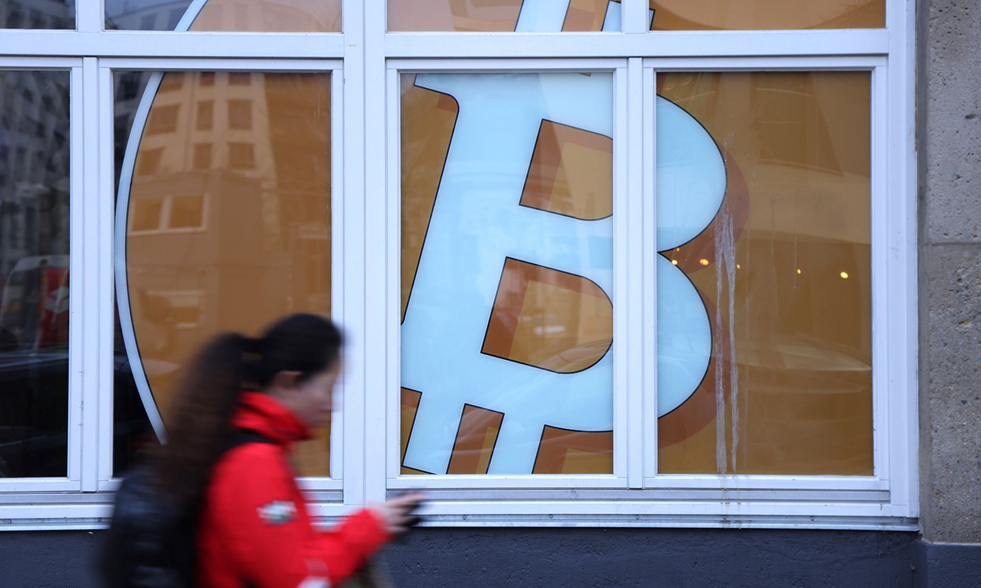 A woman walks past a Bitcoin symbol in the window of a company that offers blockchain application services on Dec. 21, 2021. in Berlin. (Photo by Sean Gallup/Getty Images)