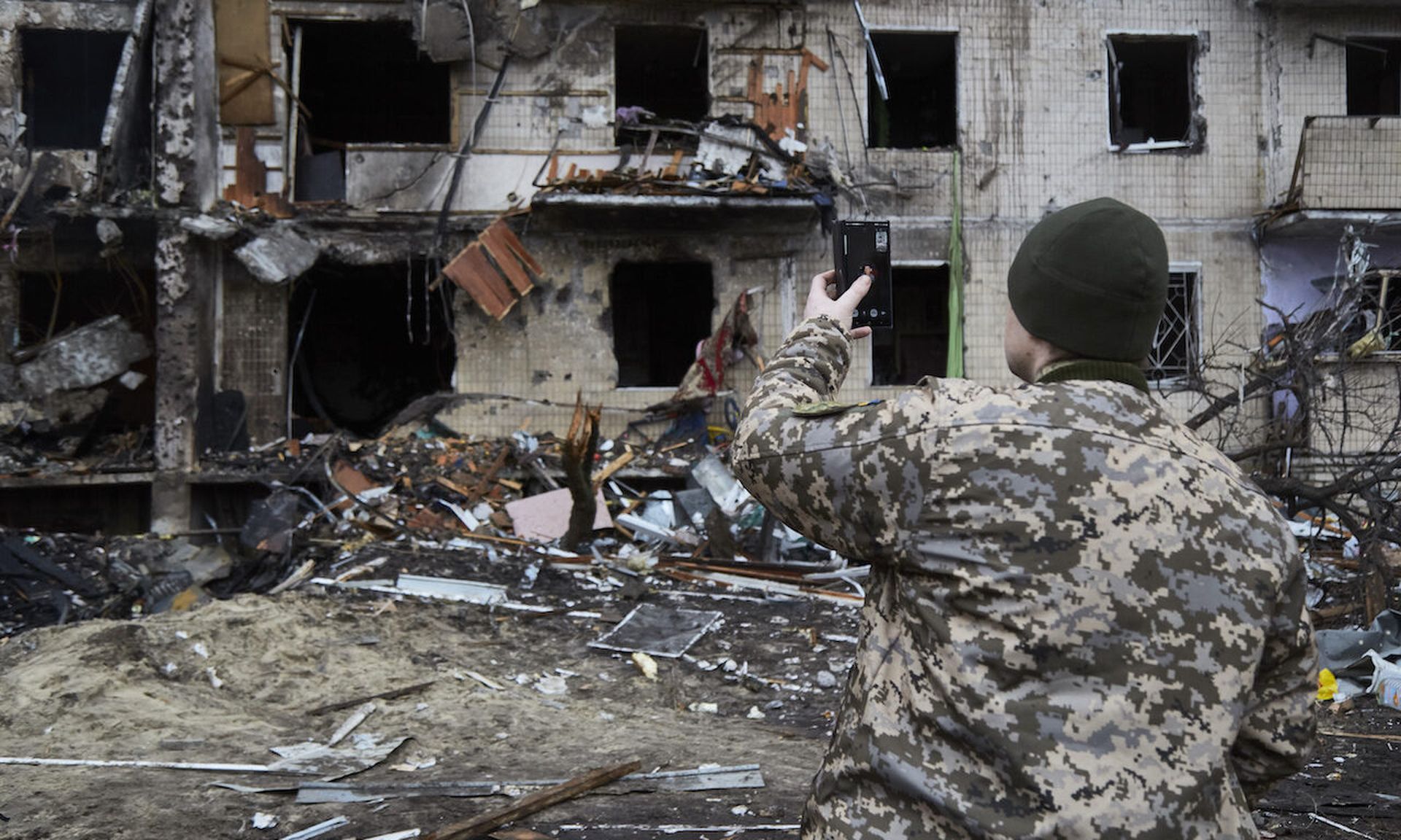 KYIV, UKRAINE &#8211; FEBRUARY 25: A Ukrainian soldier speaks on his smartphone outside a residential building damaged by a missile on February 25, 2022 in Kyiv, Ukraine. Yesterday, Russia began a large-scale attack on Ukraine, with Russian troops invading the country from the north, east and south, accompanied by air strikes and shelling. The Ukra...