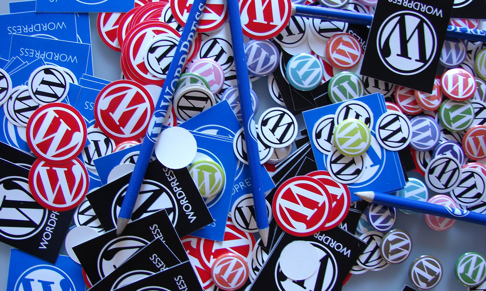 Stickers, buttons and pencils with the WordPress logo are seen in a pile.