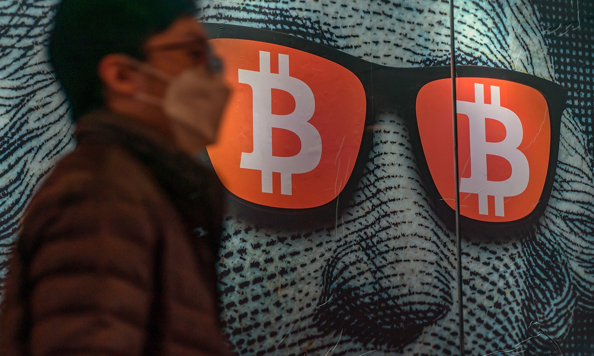 A pedestrian walks past a display of George Washington on the dollar bill wearing sunglasses with the Bitcoin logo in the lenses.