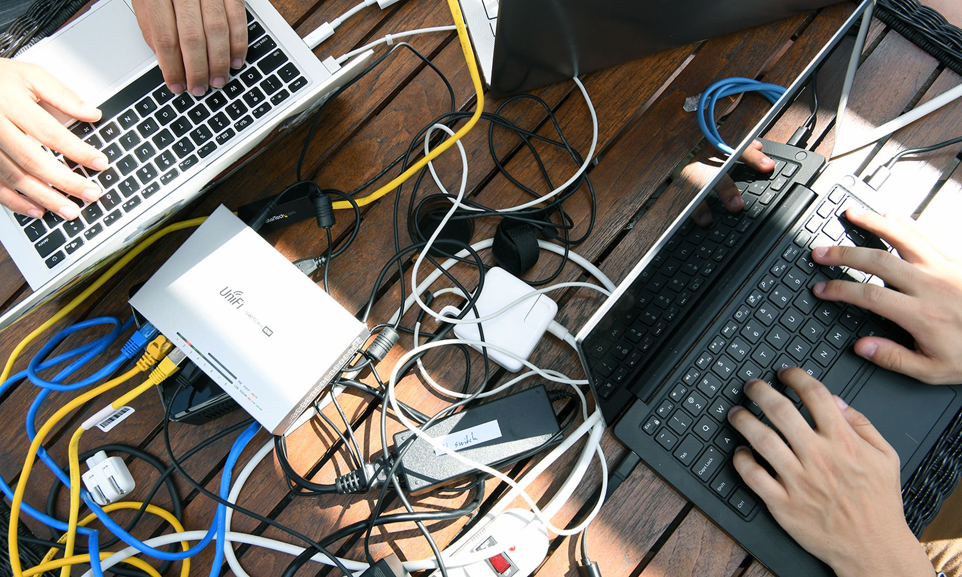 Laptops, chords and wifi and power chords are seen on a table top.