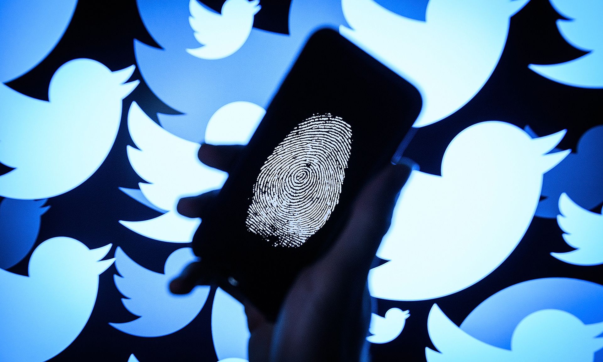 A thumbprint is displayed on a mobile phone as the logo for the Twitter social media network is projected onto a screen.