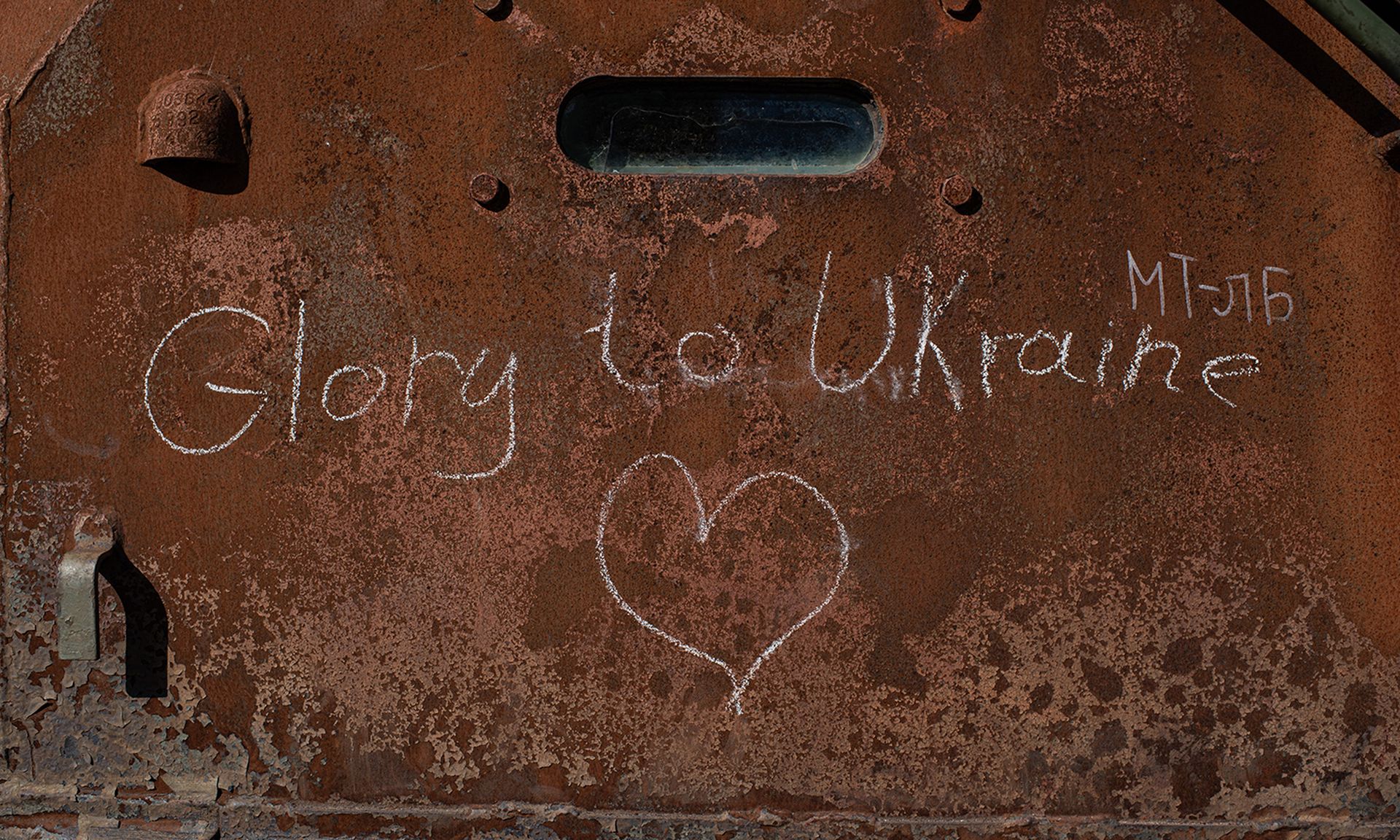 The words "Glory to Ukraine" are written in chalk on a burnt Russian military vehicle in Kyiv.