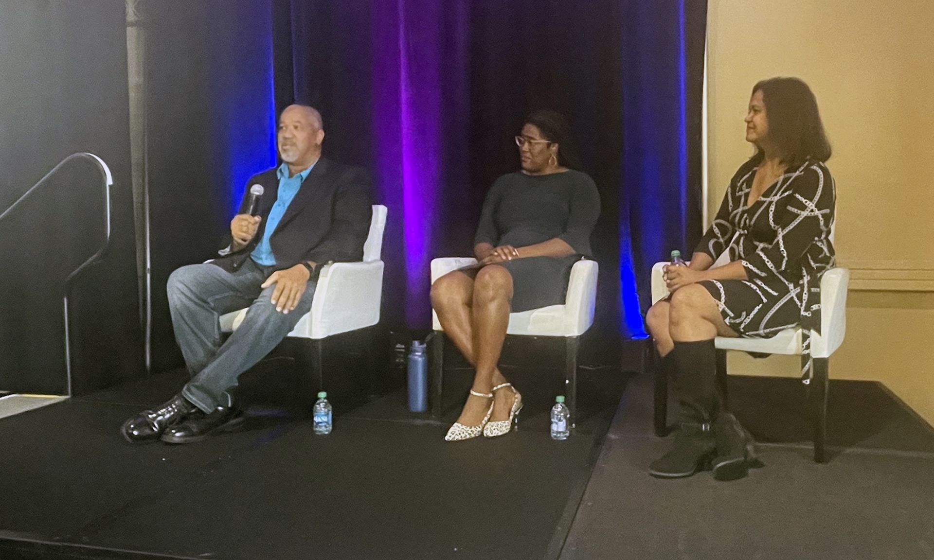 Three panelists sit on a stage