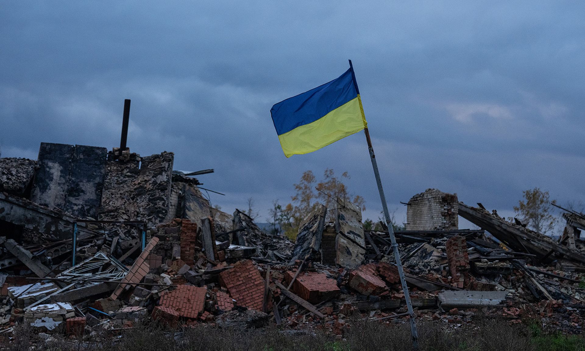 A blue and yellow Ukrainian flag flies among ruins