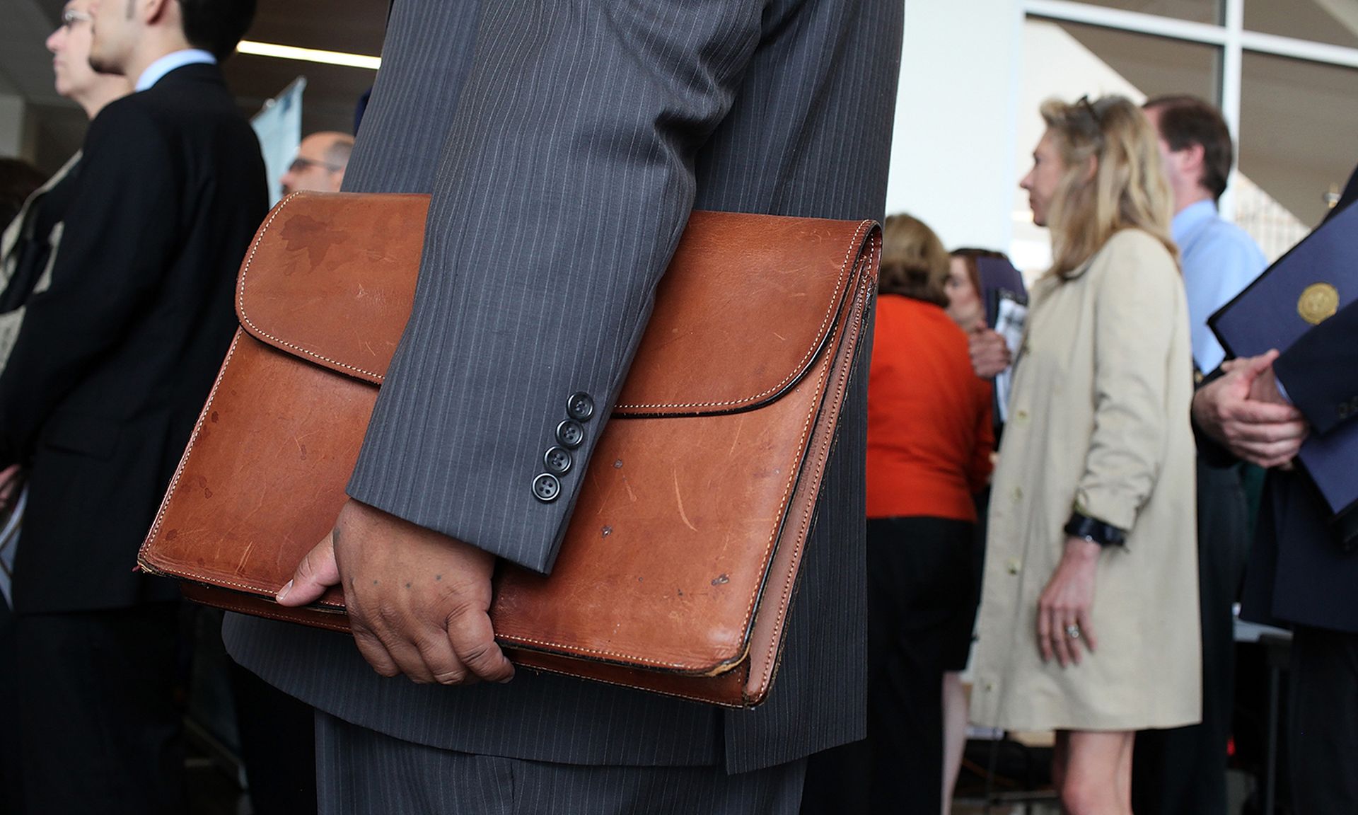 A job seeker holds a briefcase as he waits in line to meet with recruiters.