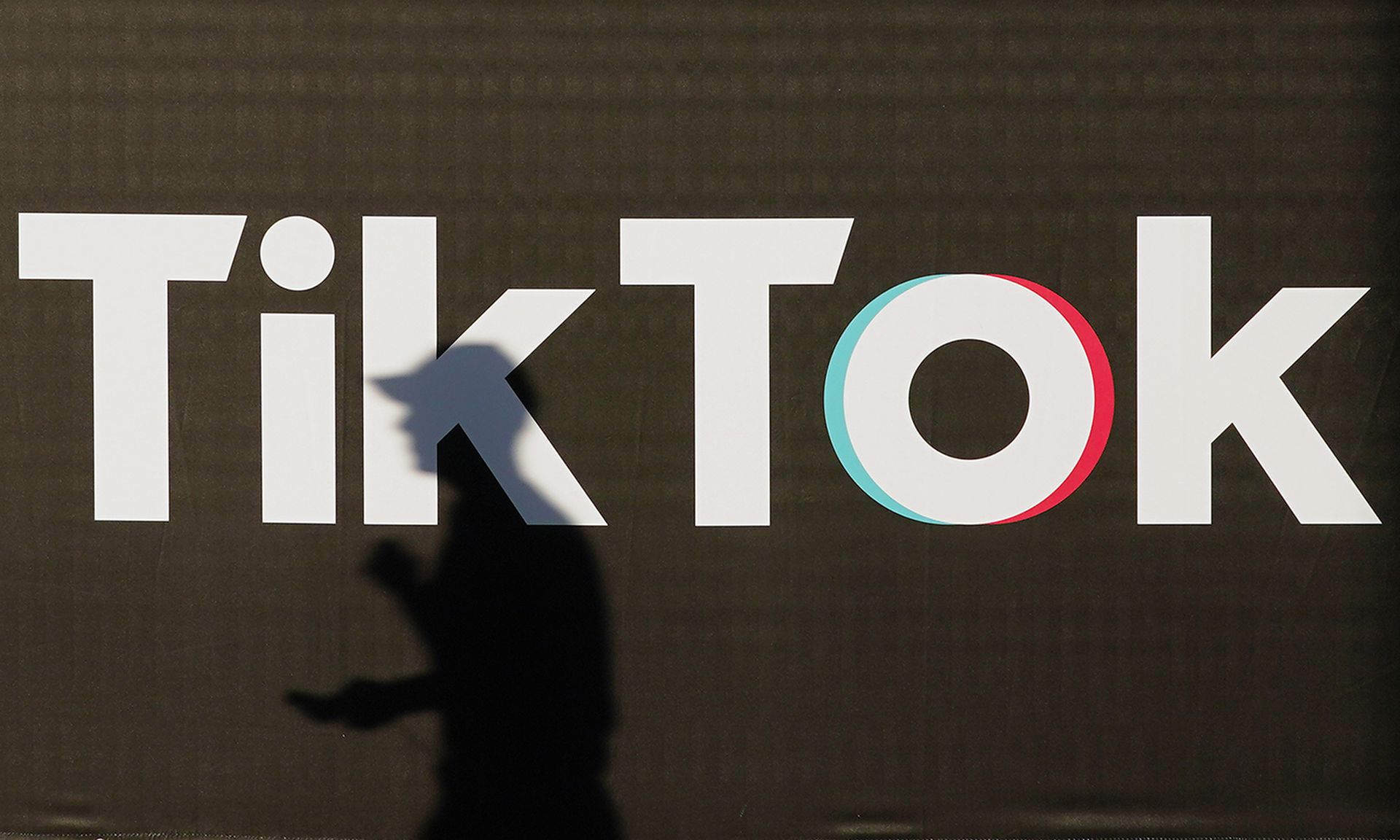 A young man holding a smartphone casts a shadow as he walks past an advertisement for social media company TikTok.