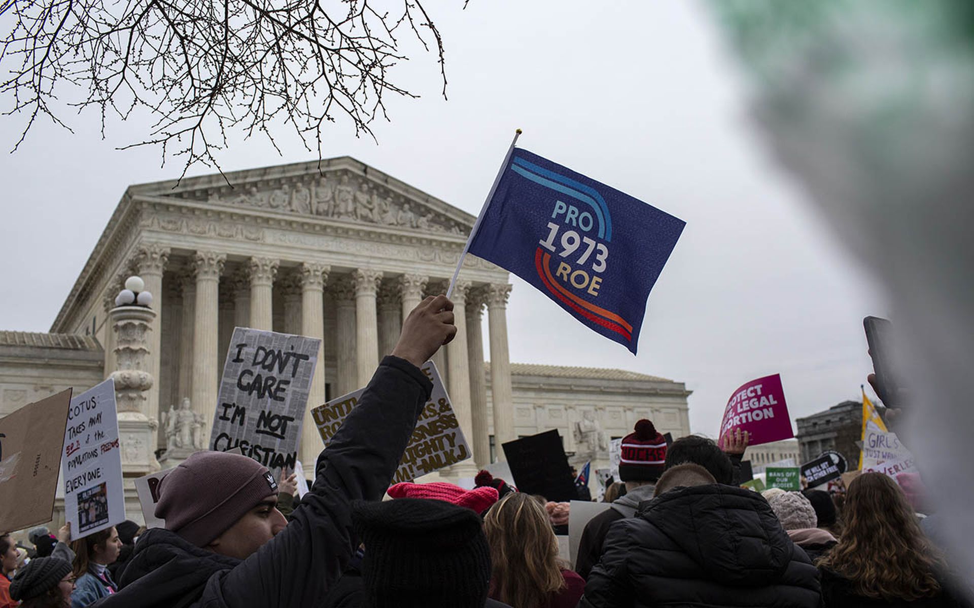 A person holds a flag that reads "Pro Roe 1973" in front of the US Supreme Court.