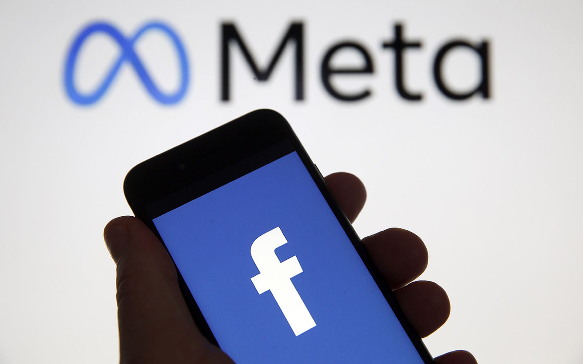 Facebook logo is seen on a smartphone in front of a Meta sign