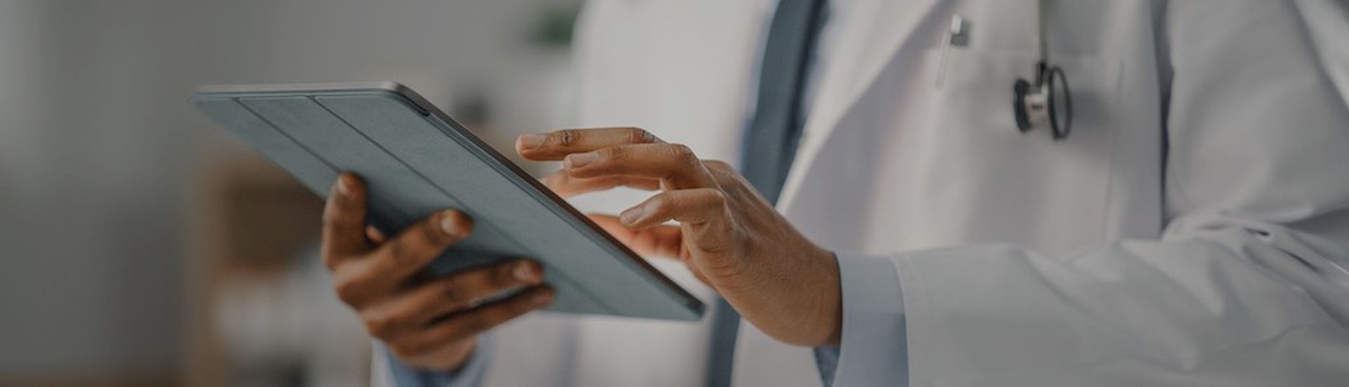 Close Up Shot of a African American Male Doctor Wearing White Coat Working on Tablet Computer at His Office. Medical Health Care Professional Working with Test Results, Patient Treatment Planning. (Close Up Shot of a African American Male Doctor Weari