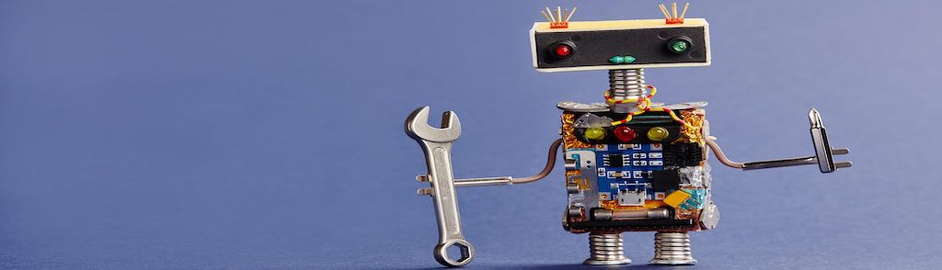 Robot serviceman with hand wrench and screwdriver on blue background. Abstract mechanical toy worker made of electronic circuits, chip capacitors vintage resistors.