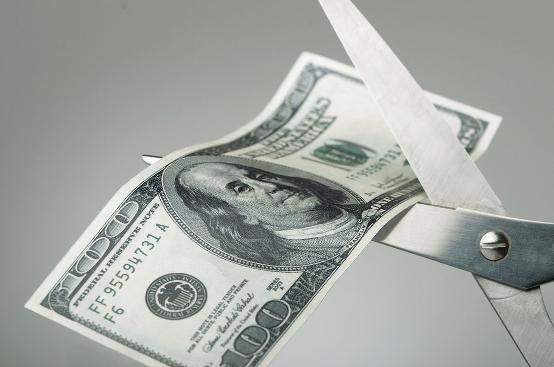 Scissors cutting a $100 bill in half