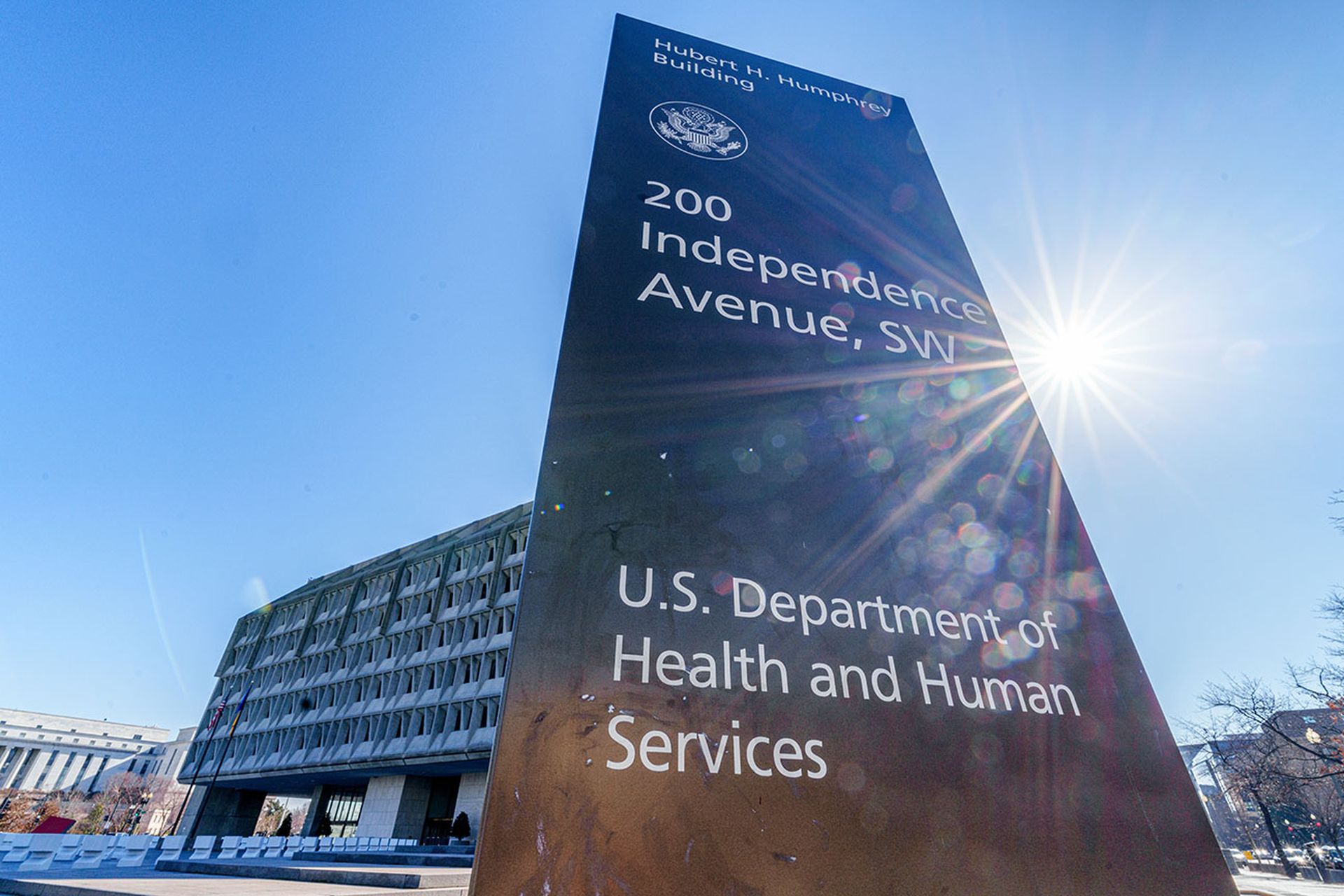 The sun flares next to the sign marking the headquarters building of the US Department of Health and Human Services