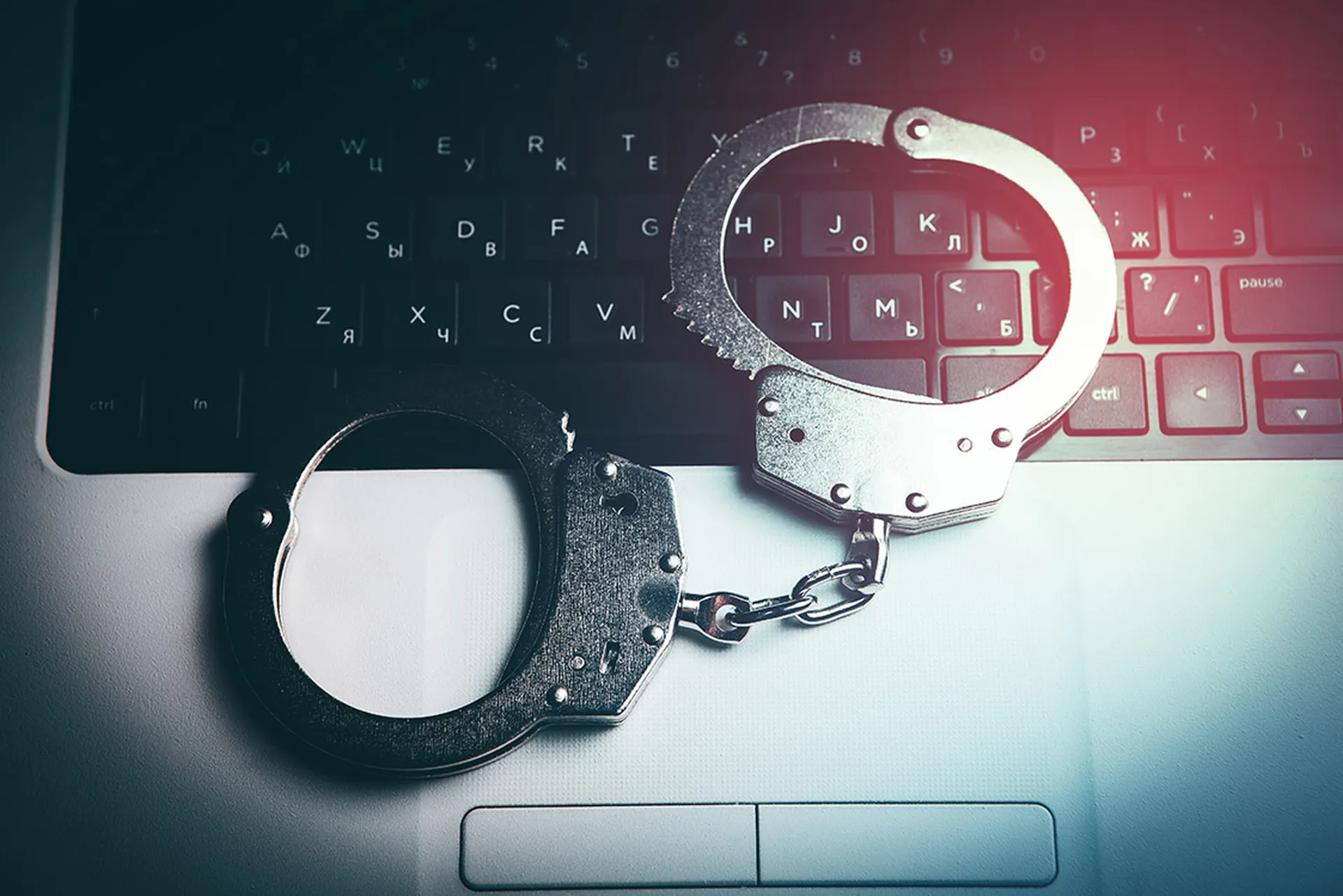 handcuffs sit on the keyboard of a laptop. cybercrime