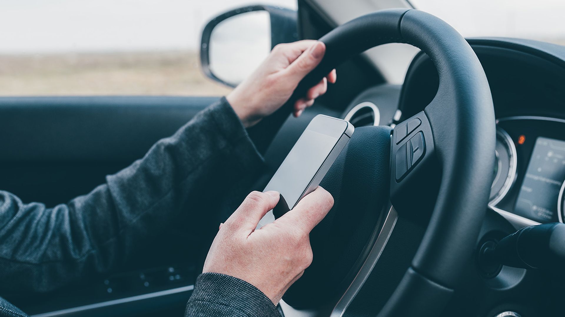 Texting and driving is dangerous behavior in traffic, close up of female hand typing text message on mobile phone while traveling through countryside with her car