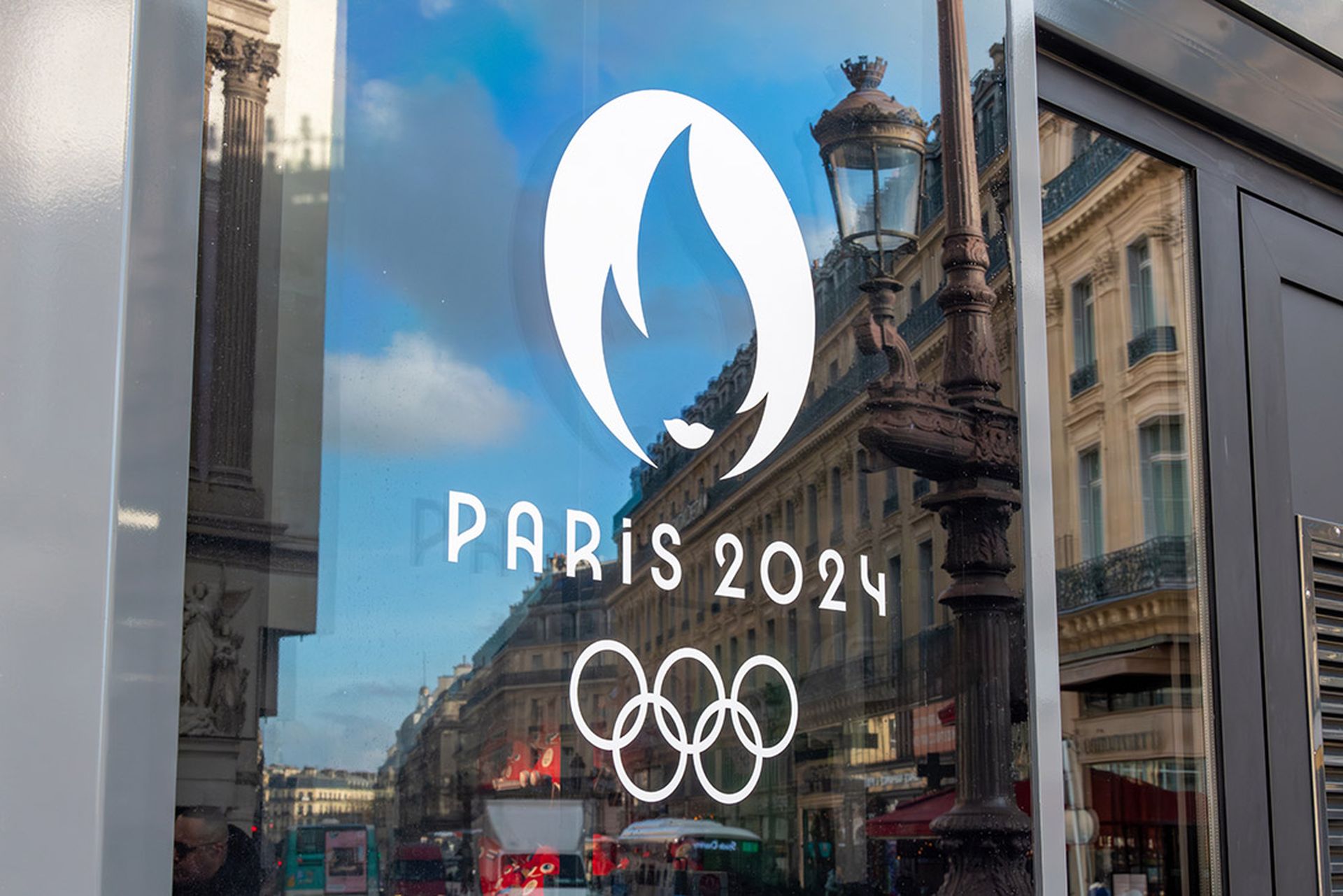 The interconnected rings of the Olympics logo and a design of the Olympic flame with the words Paris 2024 are seen on a window